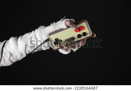 Mummy hand holding retro joystick isolated on black background. Halloween, gaming concept