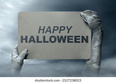 Mummy hands have dirty bandages on them. Mummy, devil, evil, satan, or zombie hands holding a piece of brown paper with a Happy Halloween sign. Happy Halloween concept - Powered by Shutterstock