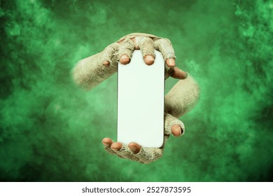 Mummy hands have dirty bandages on them. Mummy, devil, evil, satan, or zombie hands holding mobile phones or cell phones through green smokes. Mockup. Copy Space. Spooky Halloween concept - Powered by Shutterstock