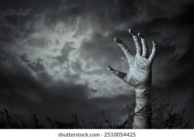 Mummy's hand wrapped in a bandage creepily moving reaches up through the ground grave. The hand of the risen dead mummy monster for Halloween horror concept