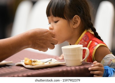 Mum's right hand was picking food on a plate to feed a girl wearing a red Chinese dress at a seminar at SD Avenue Pinklao on December 23, 2019, Bangkok, Thailand.