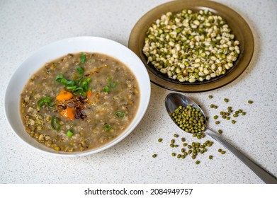 Mungo beans soup in white plate, spoon with dry mungo seed (vigna radiata), sprouted mungo in brown plate on cutting board.