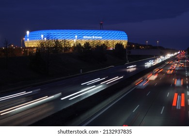 Munich, Bavaria Germany - 05.03.2022: The Football Stadium Of Bayern Munich In Blue-yellow Colors Resembling The Ukrainian Flag With Nearby Traffic At Night