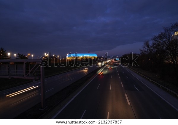 Munich, Bavaria Germany - 05.03.2022:\
The football stadium of Bayern Munich in blue-yellow colors\
resembling the ukrainian flag with nearby traffic at\
night