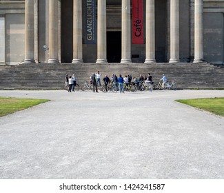 Munich, Bavaria, Germany - May 18, 2019. Tourists On Bicycles Listen To A Guide In Front Of The Antikensammlung Building In Koenigsplatz,  A Square Built In The Style Of European Neoclassicism 