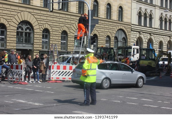 Munich, Bavaria/Germany 04.16.2019: Traffic\
lights disabled, traffic cob regulating cars, technician repairing\
lights.  Crossroad Munich Schwabing.\
