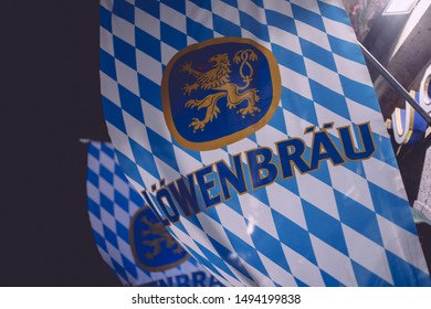 Munich, Germany - Aug. 31, 2019: Löwenbräu Brewery Bavarian Blue White Flag Hanging At House In Munich Night Dark Evening Time Illuminated