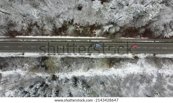 Munich, Germany\
Bavaria - April 4, 2022: Striped paved winter road winding through\
the snowy forest trees with a bike path and cars. Image taken from\
a drone at 100m\
altitude.