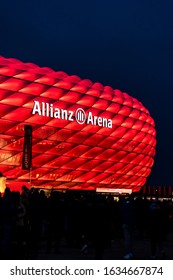 MUNICH, GERMANY - Jan 25, 2020: Illuminated Arena Of German Football Club FC Bayern MÃ¼nchen. Red Light Of Allianz Arena With Fans Walking To See The Match.