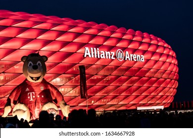 MUNICH, GERMANY - Jan 25, 2020: Illuminated Arena Of German Football Club FC Bayern MÃ¼nchen. Red Light Of Allianz Arena With Fans Walking To See The Match.