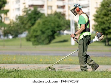 Municipal Gardener Landscaper Man Worker Cutting Grass with String Trimmer Machine along City Street