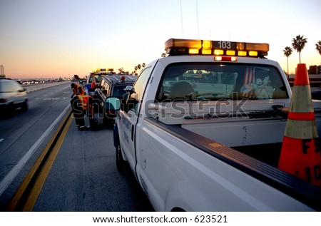 Municipal roadside assistance helping to tow away a broken car off the freeway at sunset