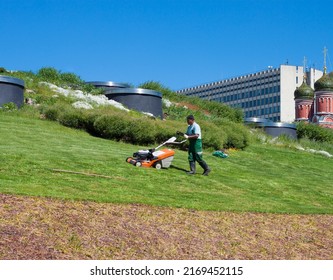 A Municipal Utility Worker, A Gardener Of The Municipality, Mows The Grass In The City Park. June 7, Moscow, Zaryadye Park