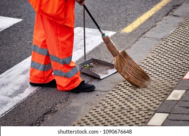 municipal worker sweep the road with broomstick and collects garbage in  scoop. sanitation worker sweep street