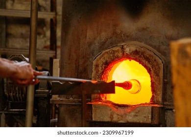 Murano glass-blowing factory. blower forming beautiful piece of glass: put iron rod with attached glass object in furnace to make the glass malleable. Venice, Italy - Powered by Shutterstock