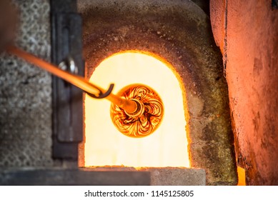 Murano glass-blowing factory. Glass blower forming beautiful piece of glass: put iron rod with attached glass object in furnace to make the glass malleable. Venice, Italy - Powered by Shutterstock