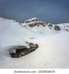 Muratov peak and thawed patch at Muratovo lake in spring cloudy day during snowmelt. Dark stormy clouds over the snow covered mountains. Pirin national park near Bansko, Bulgaria. - Powered by Shutterstock