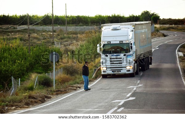 Murcia, Spain, December 5,\
2019: Man talking on the phone about to be hit by a truck. Possible\
collision in the road. Imminent death or accident by truck\
collision