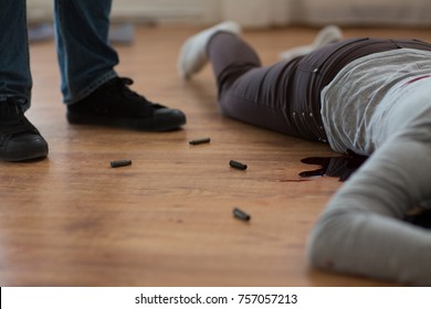 Murder, Kill And People Concept - Criminal Or Murderer With Bleeding Dead Woman Body Lying On Floor And Bullet Sleeves At Crime Scene