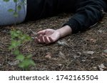 Murder in the woods. The hand of a dead woman in a tracksuit lies in the forest on the ground. The concept of violence against women. Horizontal photo. Close up.