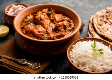 Murgh Makhani / Butter chicken tikka masala served with roti / Paratha and plain rice along with onion salad in terracotta crockery. selective focus