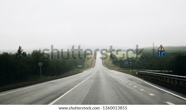 Murmansk region - August 2018: Panoramic view of the\
misty asphalt road in rainy weather. Foggy winding highway\
surrounded by mountains and hills in Kola Peninsula. Summer morning\
road and fog. 