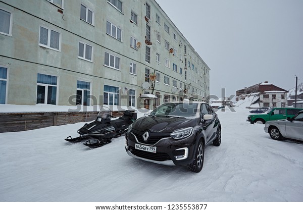 Murmansk\
Region, Russia - March 2018: Renault Captur  in a winter landscape,\
next to a snowmobile, in cloudy gray\
weather
