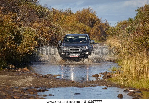 Murmansk region, Russia - September 2018: A\
pick-up truck to Isuzu d-max is wade across a river, splashes of\
water are flying against the backdrop of a beautiful autumn forest.\
Off road tourism