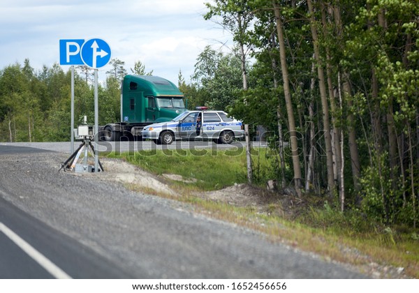 MURMANSK, RUSSIA-CIRCA\
JUL, 2015: Speed control radar with tripod stands on roadside.\
Russian road police car is hidden at the turn. Mobile speed camera\
is on Kola highway