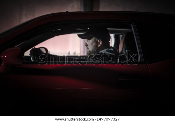 Muscle Car Night Drive. Young Caucasian Men in His\
20s Wearing Black Baseball Hat Driving His Car Late Night Hours.\
Transportation Theme.