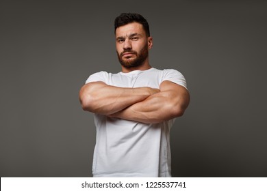 Muscle Concept - Suspicious Young Man With Crossed Big Muscular Arms Showing His Arrogant Strength And Male Power, Looking Down At Camera