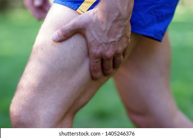 Muscle Injury -  Man With Sprain Thigh Muscles After Jogging In Park. Athlete In Sports Shorts Clutching His Thigh Muscles.