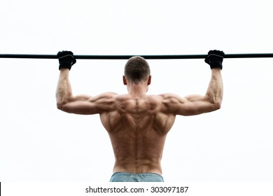 Muscle man making pull-up on horizontal bar against the sky