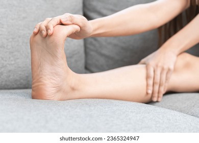 Muscle pain or leg pain, suffer asian young woman, girl hand massaging brawn foot muscle cramps or spasm, trauma from inflammation of tendon at feet while sitting on sofa. Health care concept.