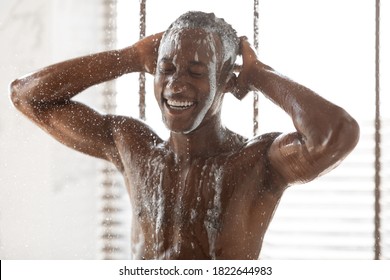 Muscular African American Man Washing Hair And Body Using Male Shampoo Taking A Shower Standing Under Hot Water In Modern Bathroom At Home. Men's Beauty Routine And Hygiene Concept