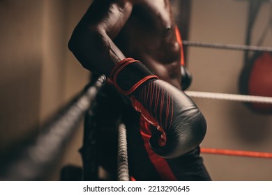 Muscular African boxer resting against the ropes of a boxing ring in a gym. Sweaty young man taking a break from training in a fitness gym. - Powered by Shutterstock