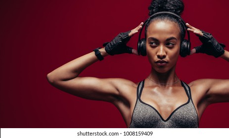 Muscular African Female With Headphones On Red Background. Fitness Woman Relaxing And Listening Music During Her Workout.