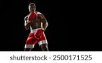 Muscular African man, boxer in red gloves and shorts stands in a defensive stance, ready for action isolated on black background. Concept of professional sport, active lifestyle, body, strength