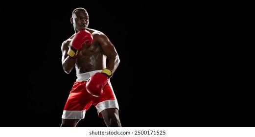 Muscular African man, boxer in red gloves and shorts stands in a defensive stance, ready for action isolated on black background. Concept of professional sport, active lifestyle, body, strength - Powered by Shutterstock