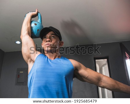 A muscular asian man does kettlebell overhead press. Upper body and shoulder workout at the gym.