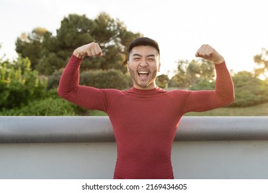 Muscular Asian man flexing biceps with both arms outdoors at sunset
