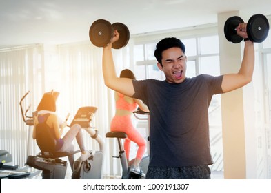 Muscular Asian Young Handsome Man Powerful Shouting Screaming And Doing Exercises With Dumbbell At Biceps In Fitness Gym, Bodybuilder, Healthy, Exercise Fitness, Workout And Sport Training Concept