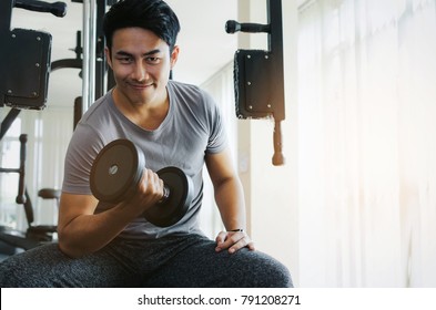 Muscular Asian Young Handsome Man Smiling And  Doing The Exercises With Dumbbell At Biceps In Fitness Gym, Bodybuilder, Healthy Lifestyle, Exercise Fitness, Workout And Sport Training Concept