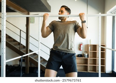 Muscular athlete performing pull-ups, developing back strength during intense cross-training session in urban outdoor fitness environment