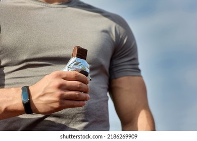 Muscular athlete rests after a workout, an athlete eats a protein bar. A young athlete eats an energy bar while enjoying chocolate after a hard workout at the stadium - Powered by Shutterstock