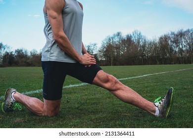 Muscular Athlete Stretching Body In A Yoga Position Pose On A Field During Lockdown. Cinematic Filter. Runner Preparing For A Workout Session In Winter.