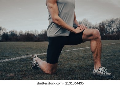 Muscular Athlete Stretching Body In A Yoga Position Pose On A Field During Lockdown. Cinematic Filter. Runner Preparing For A Workout Session In Winter.