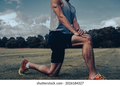 Muscular Athlete Stretching Hamstring And Hip Flexor In A Yoga Position On A Field During Lockdown. Cinematic Filter. Runner Preparing For A Workout Session.