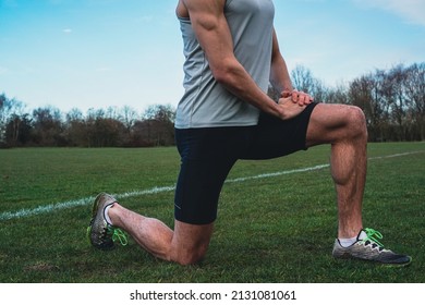 Muscular Athlete Stretching And Warming Up In A Yoga Position Pose On A Field During Lockdown. Cinematic Filter. Runner Preparing For A Workout Session.