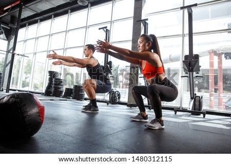 A muscular athletes doing workout at the gym. Gymnastics, training, fitness workout flexibility. Active and healthy lifestyle, youth, bodybuilding. Doing exercises together, training in squats.
